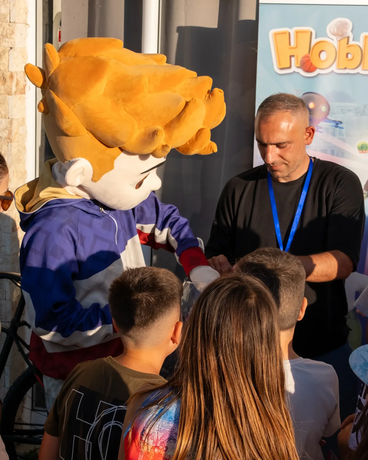 Παιδιά διασκεδάζουν με τη μασκότ του φροντιστηρίου σε εκδήλωση αγγλικών.